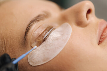Close-up of eyelash care treatment procedures. Beautiful female, blond hair model have eyelashes...