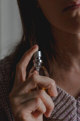 Perfume bottle in a woman's hand. Woman sprinkles perfume on her neck