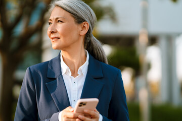 Grey asian woman wearing blue jacket using mobile phone