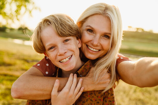 White mother and son smiling while taking selfie photo on field