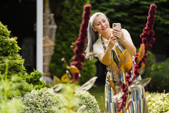 Mature woman taking photo on cellphone while working in her garden