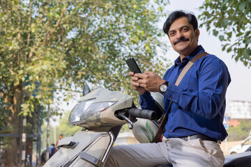 Man in formal clothing using mobile while sitting on scooty