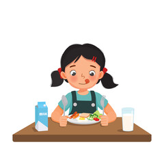 Cute little girl feeling excited eating breakfast with bread, fried egg, broccoli, vegetables, milk holding spoon and fork.