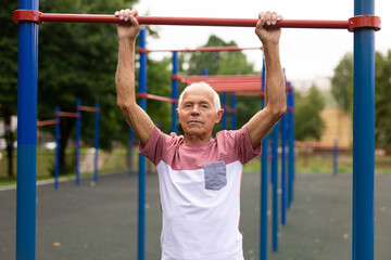 Obraz premium Active grandpa pulls up on horizontal bar on sports ground