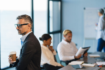 Grey man drinking coffee during meeting at office