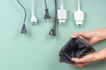 Many power cable cords hanging over empty open wallet in woman hands. Electric power consumption,...