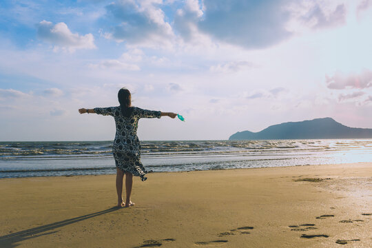 Woman holding protective mask in her hand standing on the beach for fresh air.