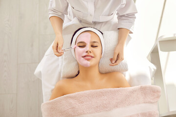 Top overhead view of beautiful young woman or teenage girl on soft towel in beauty parlor or spa salon enjoying calming soothing pampering French rose pink kaolin clay facial mask for fresh clear skin