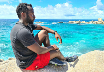 A man siting and relaxing on a rock at the seaside