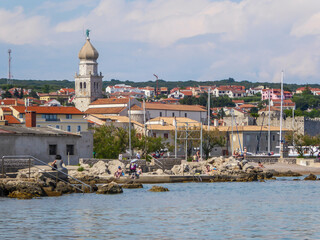 Shore line of city center of Krk Croatia. Facilities enabling the entrance to the sea. In the back there is a church tower. Few yachts parked in the port. There is a forest in the back. Gloomy weather