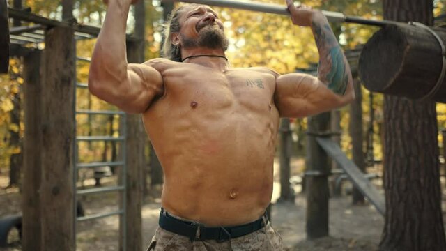 Athletic man doing overhead deadlift with barbell. Workout in the forest gym, outdoors
