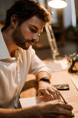 White man writing down notes in planner while working at office