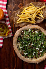 Mushrooms and rocket salad gourmet pizza in a modern italian restaurant, two boats of french fries a side