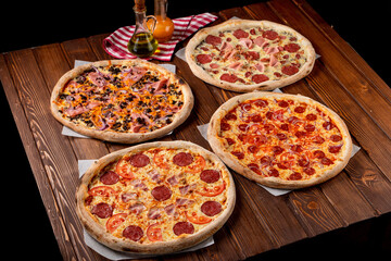 Four different pizzas served on wooden dark italian bistro table, pepperoni pizza, ham pizza,...