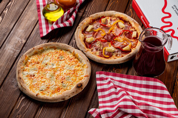 Four cheese pizza and whole round pineapple pizza in an italian pizzeria, top view, oil and sauce aside, delivery box on background