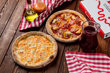 Four cheese pizza and whole round pineapple pizza in an italian pizzeria, top view, oil and sauce aside, delivery box on background