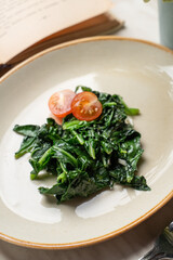 Sauteed spinach garnish, served on clay plate with book and cutlery aside, top view with copy scape for menu