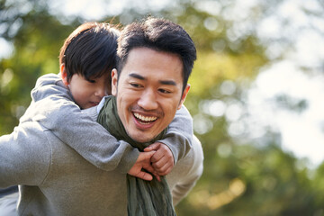 asian father and son having fun outdoors in park - obrazy, fototapety, plakaty