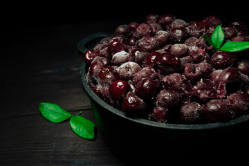 Frozen cherry in a bowl with green leaf on wooden black background.Vitamins and a healthy diet