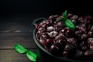 Frozen cherry in a bowl with green leaf on wooden black background.Vitamins and a healthy diet