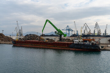 harbor crane unloading scrap metal from a freight ship in the industrial port of Ploce
