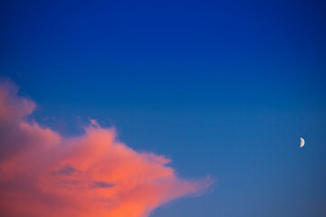 Colorful orange cloud against blue sky with a half moon at sunset, lots of copy space.
