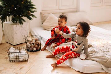 Multi-racial African American little curly-haired children in Christmas pajamas and Santa Claus hats are playing opening gifts in anticipation of the holiday in the New year vacations. Selective focus