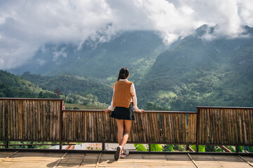 Asian woman standing and enjoying the mountain view on wooden balcony in sunny day