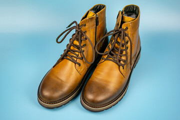New pair of winter leather boots on a light blue background. View from above. Fashionable concept.