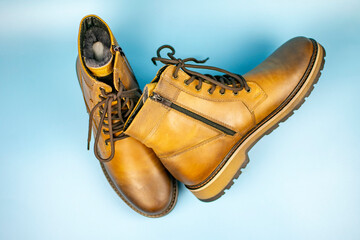 New pair of winter leather boots on a light blue background. View from above. Fashionable concept.