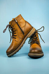 New pair of winter leather boots on a light blue background. One shoe is located on top of the other, front view. Fashionable concept.