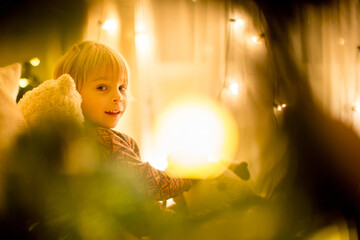 Cozy christmas atmosphere at home, child sitting on the bed, reading a book, enjoying christmas ligths and cup of tea