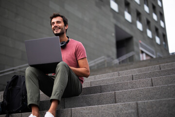 Handsome man working with laptop on city street. Man using his laptop while sitting on stairs outdoors..