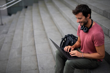 Handsome man working with laptop on city street. Man using his laptop while sitting on stairs outdoors..