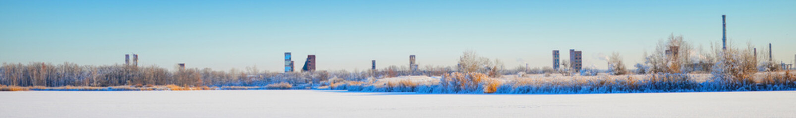 An abandoned old chemical plant on the bank of a frozen winter river covered with snow. Industrial winter landscape