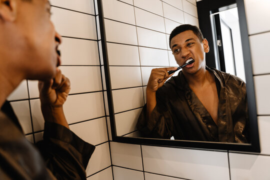 Black man wearing bathrobe brushing his teeth in bathroom