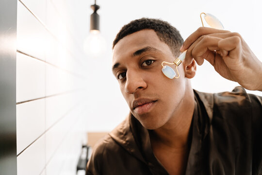 Black Man Wearing Bathrobe Massaging Face With Jade Roller