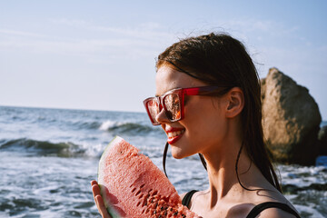 cheerful woman in black swimsuit eating watermelon on the beach