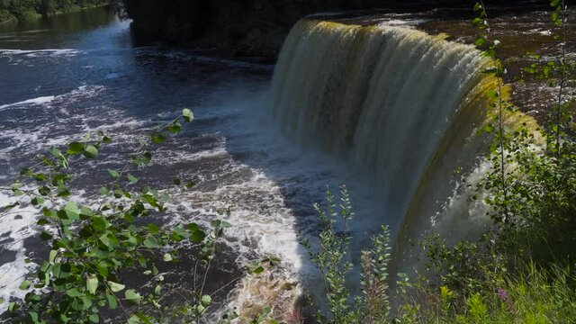 Waterfall at drop-off point of Higher Falls of Tahquamenon Falls; side view of full length of water falling into pool below. 