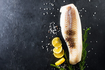Fillet of white cod fish on a dark background with lemon, ice and coarse sea salt.