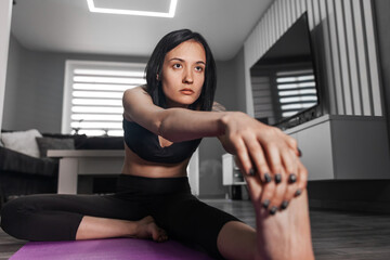 Focused young woman doing leg stretch exercise at home