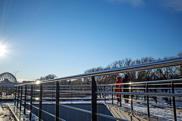 A man and a woman in warm clothes walk along the city embankment on a sunny winter day