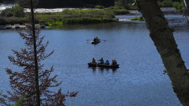 Two rowboats on a blue river in late afternoon light with trees and inlets in the background. 