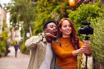 Fototapeta premium Young Couple Travelling Through City Together Vlogging To Video Camera On Handheld Tripod