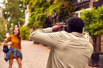 Woman Posing And Man Taking Photos On Camera As Young Couple Travel Through City Together