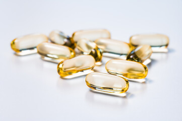 Golden yellow soft capsules reflecting light on white background. Medicine, drug, dietary or...