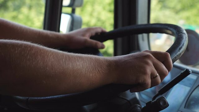 Male hands of lorry driver holds a big steering wheel while driving a truck at summer day. Trucker riding to destination at country road. Concept of logistics and transportation. Close up Slow mo