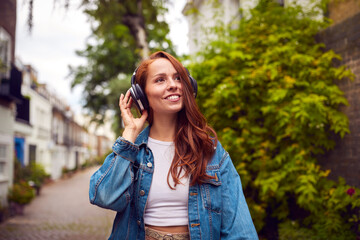 Female Vlogger Or Social Influencer Wearing Headphones Travelling Through City