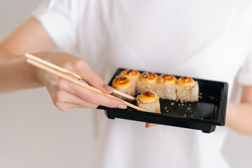 Close-up hands of unrecognizable young woman taking fresh sushi rolls with chopsticks on white isolated background in studio. Pretty Caucasian female eating Asian food.