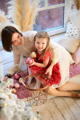 The Cute little girl in a beautiful red dress with a Christmas balls in the hands helps her mother are decorating a Christmas tree in the house. Merry Christmas! family, winter holidays concept